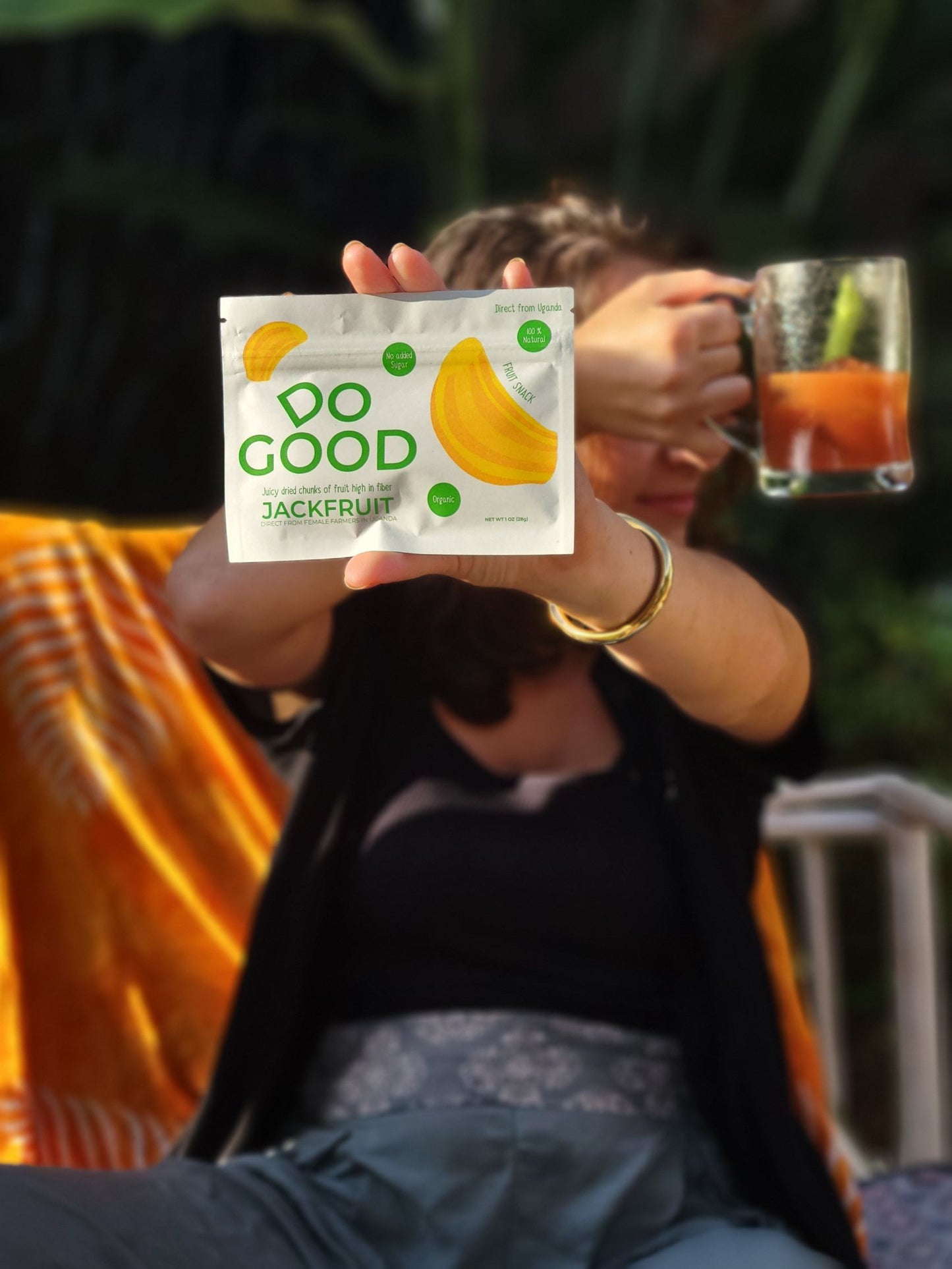 Woman holding DoGood organic jackfruit snack pack with a drink outdoors