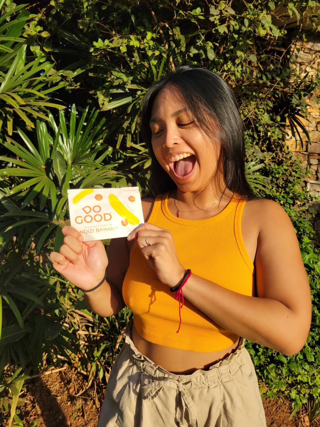 Smiling woman enjoying DoGood Ndizi Banana organic dried fruit snack outdoors, healthy natural no added sugar treat