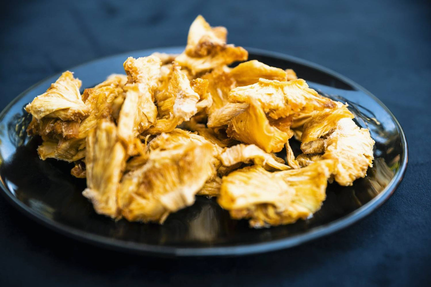 Close-up of DoGood organic dried pineapple chunks on a black plate, natural fruit snack with no added sugar