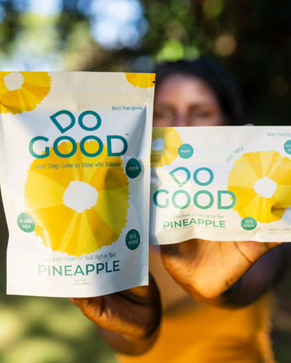 Person holding two DoGood organic dried pineapple snack packs with bright yellow fruit design, highlighting healthy no added sugar fruit snacks from Uganda